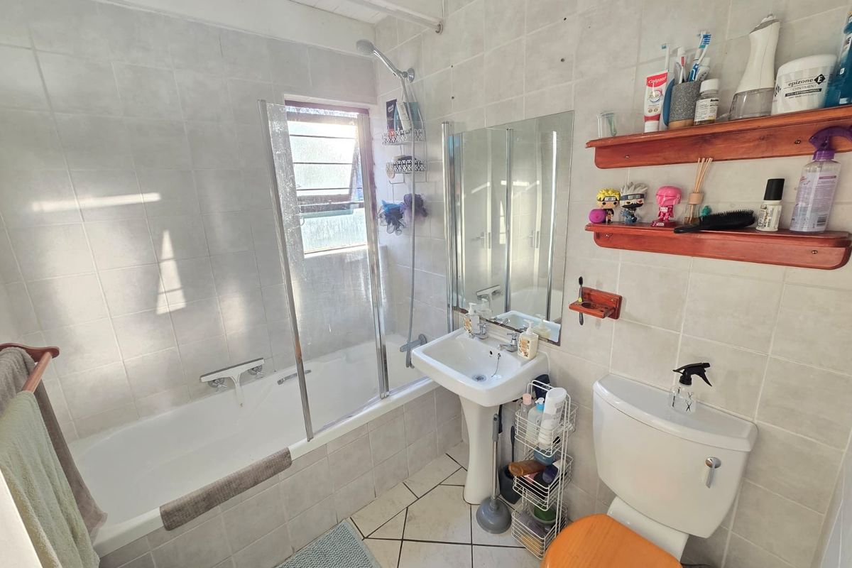 A functional bathroom featuring a pedestal basin, bathtub with a glass shower screen, and ceramic tiling throughout.