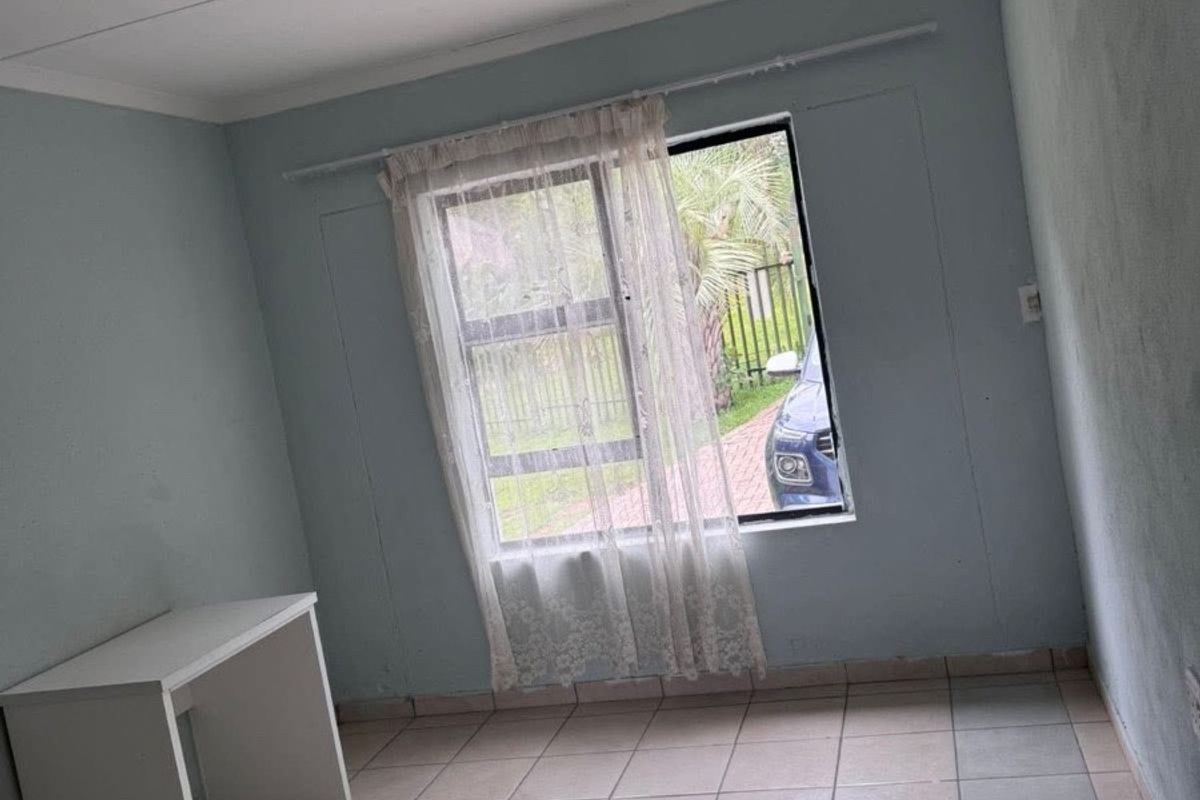 A vacant bedroom featuring tiled flooring and a window with security bars, offering a blank canvas for potential interior updates.
