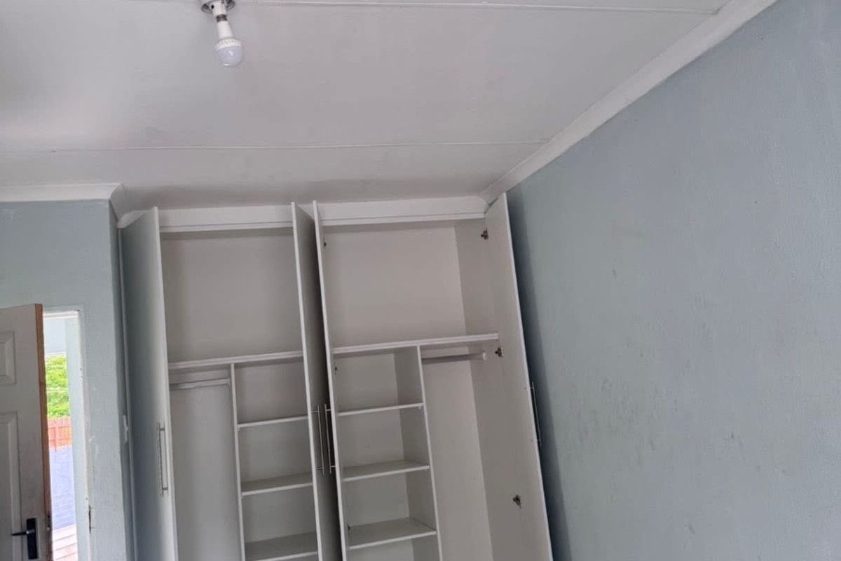 A bedroom featuring built-in white cupboards, tiled flooring, and light blue painted walls. The space is currently vacant and ready for personal touches.