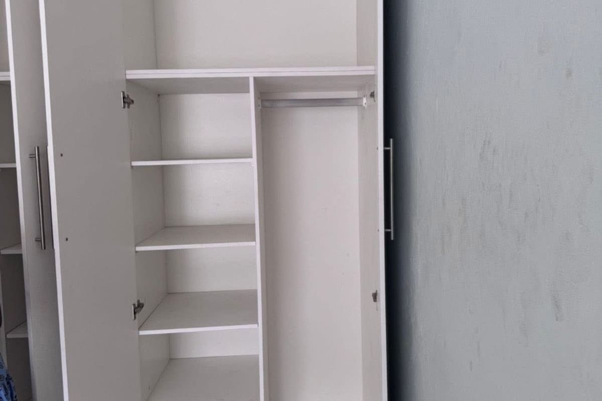A bedroom featuring a white built-in wardrobe with shelving and hanging space, complemented by tiled flooring.
