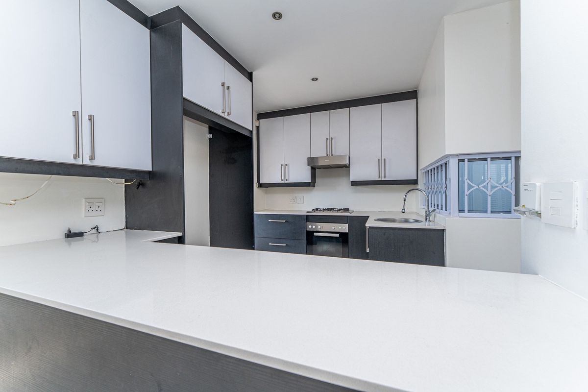 Modern kitchen featuring sleek two-tone cabinetry, stone countertops, integrated stainless steel oven, gas hob, and extractor fan in a clean, functional layout.