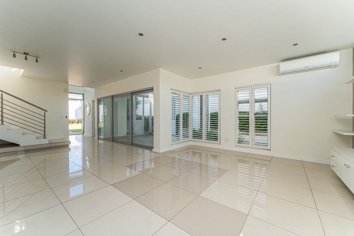 Spacious, light-filled living area featuring polished porcelain tiles, modern staircase, plantation shutters, and integrated air conditioning, offering a clean, contemporary aesthetic.