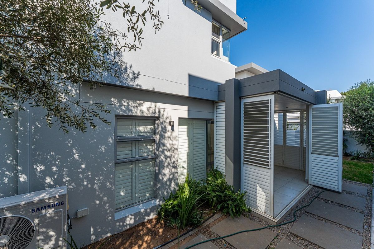 A modern rear exterior view featuring a paved patio area, integrated louvre shutters, and a well-maintained building facade with an external air conditioning unit.