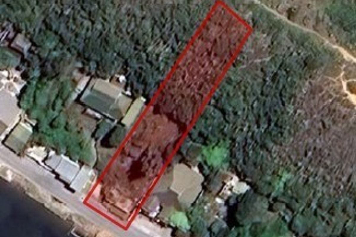 Aerial view of a vacant residential land plot highlighted in red, situated in a coastal or riverfront neighborhood.