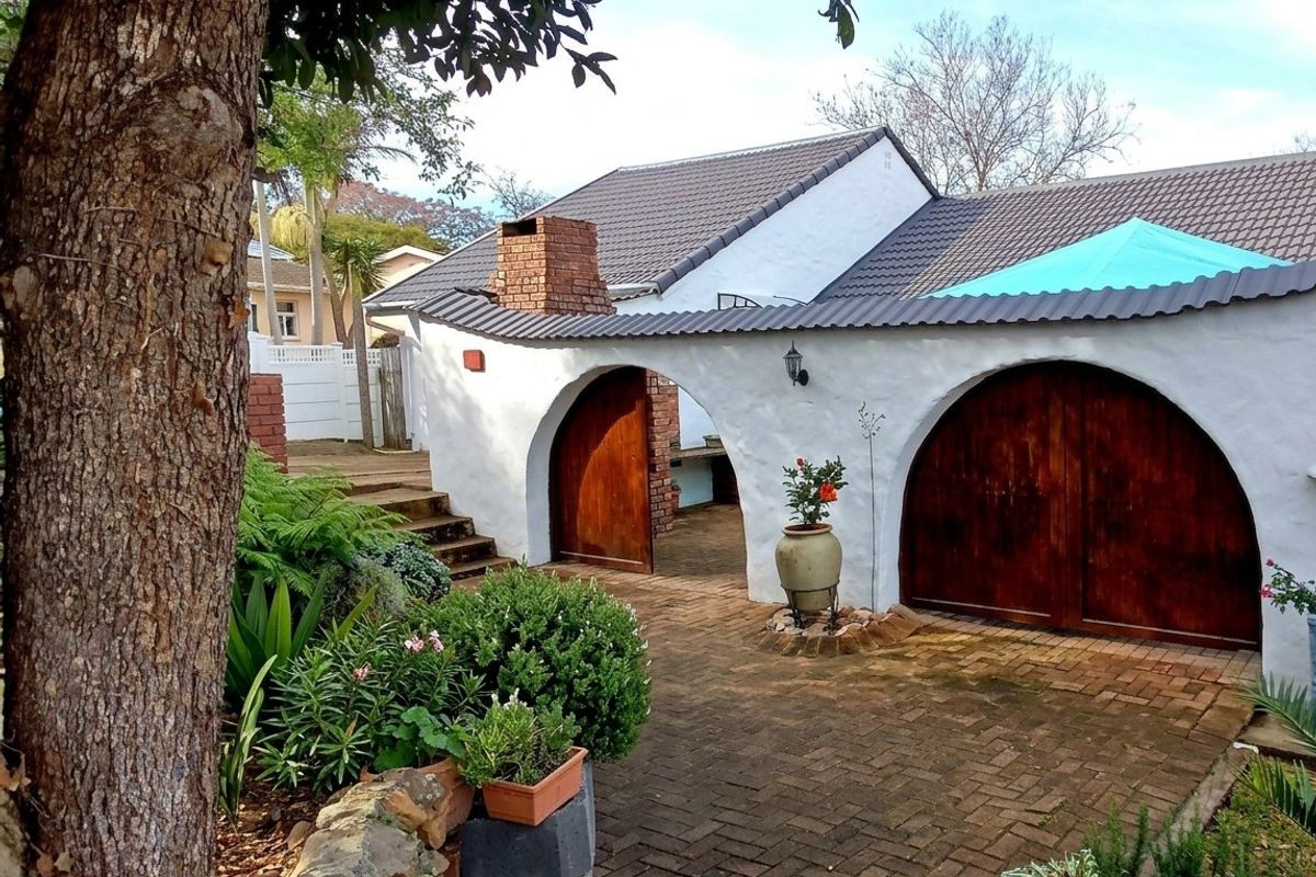 A charming rear courtyard featuring a brick-paved patio, arched wooden entryways, and a traditional brick chimney, set within a landscaped garden area.
