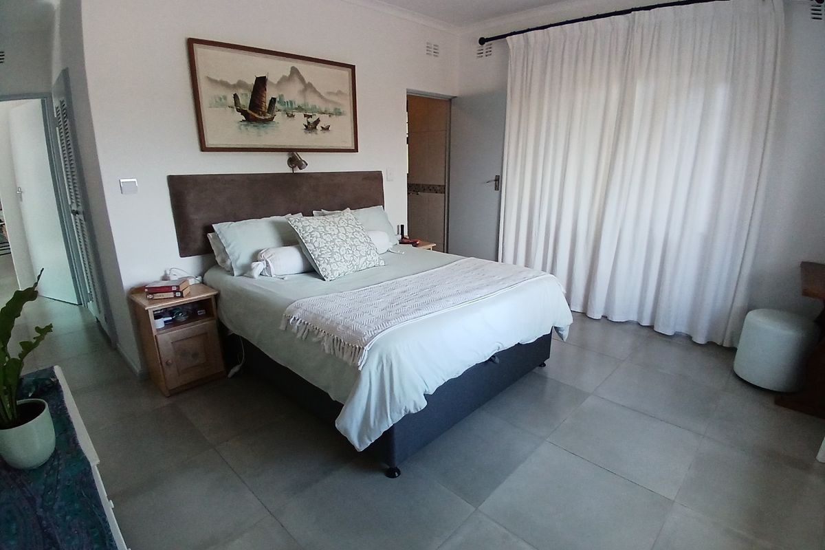 A well-maintained bedroom featuring neutral tiled flooring, white walls, and large window curtains, providing a clean and functional living space.