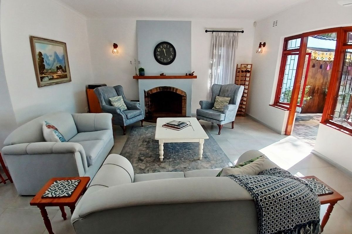 A bright living room featuring a central brick fireplace with a wooden mantelpiece, tiled flooring, and direct access to an outdoor patio area.