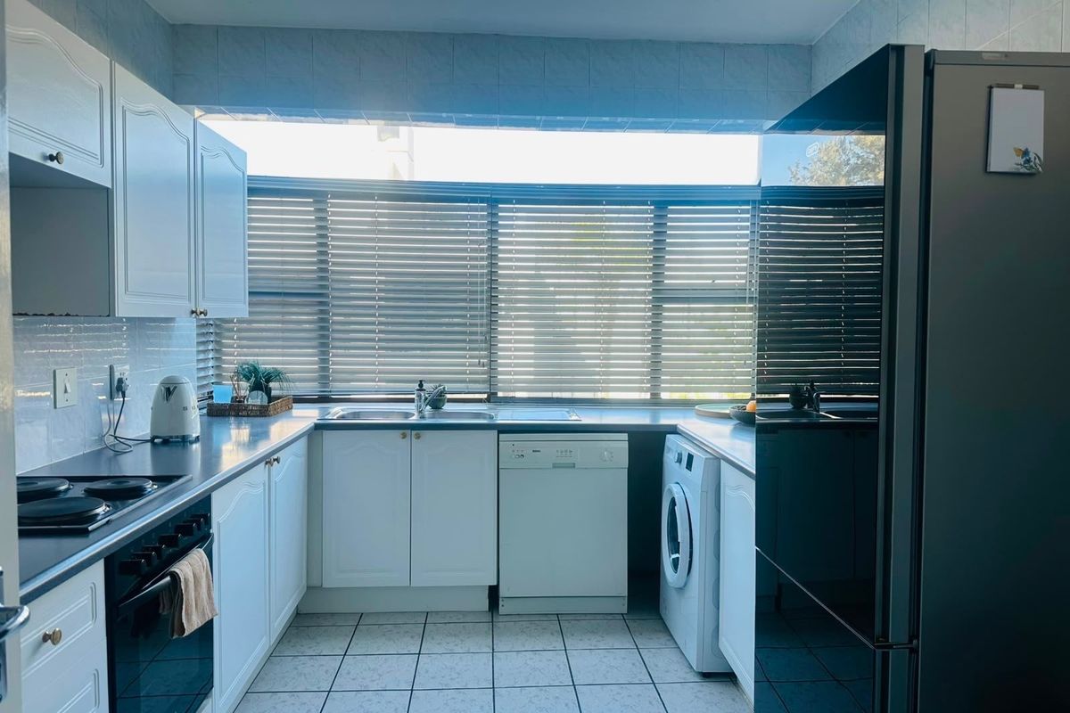 A functional kitchen featuring white cabinetry, tiled flooring, a built-in oven and hob, and large windows with venetian blinds providing natural light.