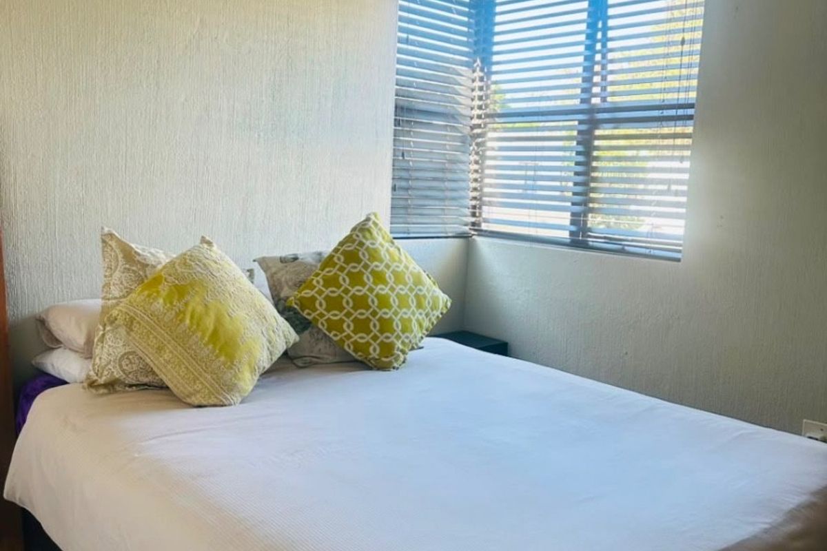 A bedroom featuring tiled flooring and corner window with fitted venetian blinds, offering a functional and well-lit space.