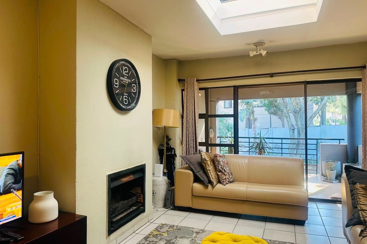 A bright living room featuring a built-in fireplace, tiled flooring, and a large skylight, with direct access to an outdoor balcony through sliding glass doors.