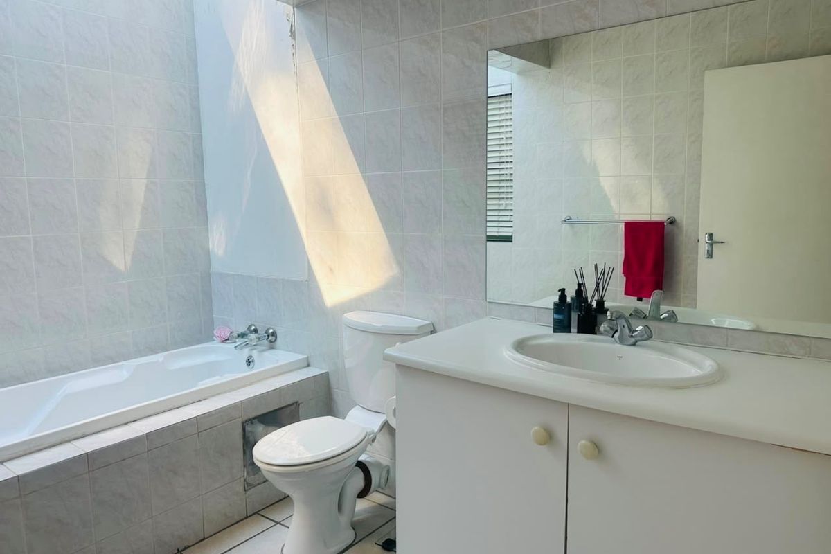 A functional bathroom featuring a built-in bathtub, vanity cabinet with integrated sink, and tiled finishes, illuminated by natural light from a skylight.