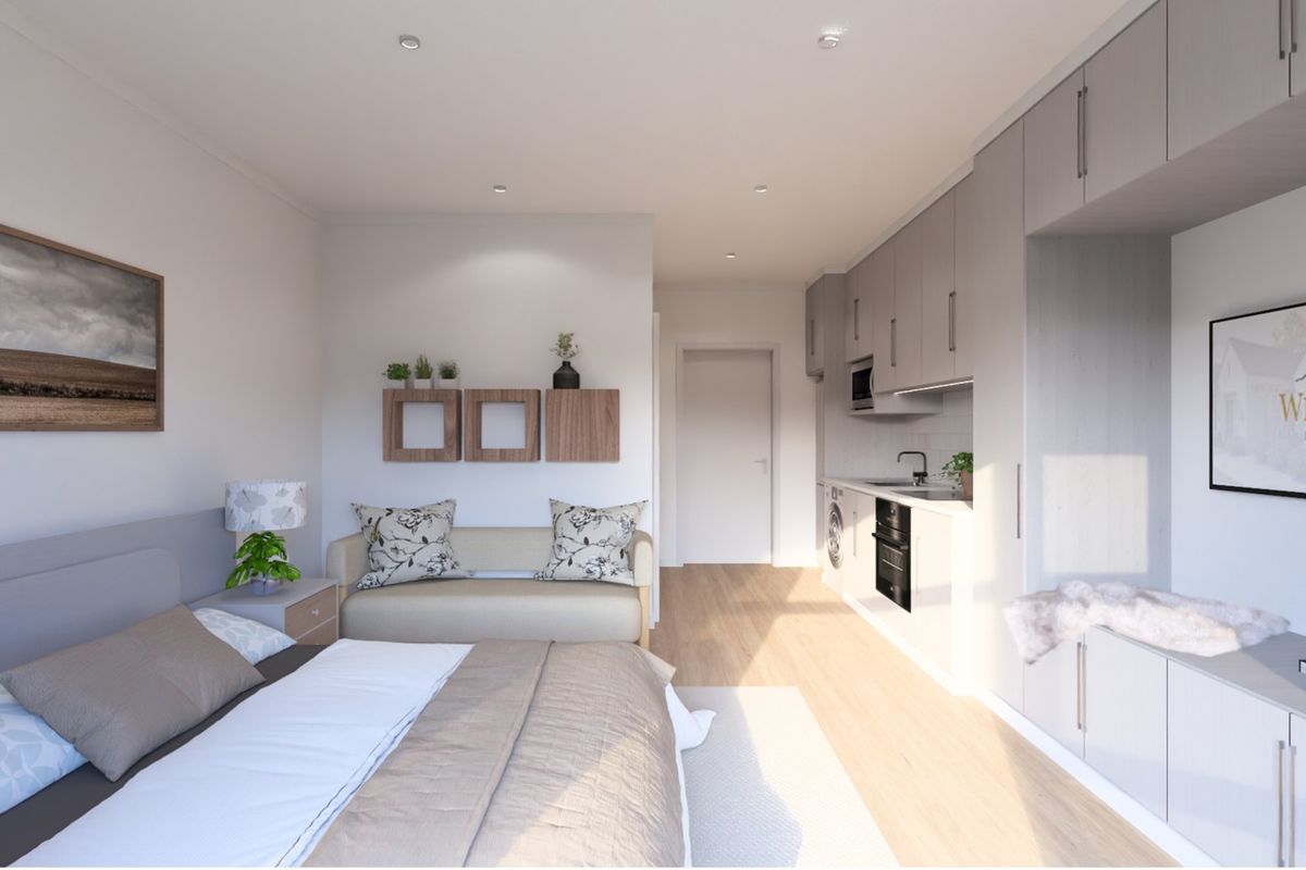 Modern open-plan studio apartment featuring a compact kitchenette with integrated appliances, neutral finishes, and efficient use of space.