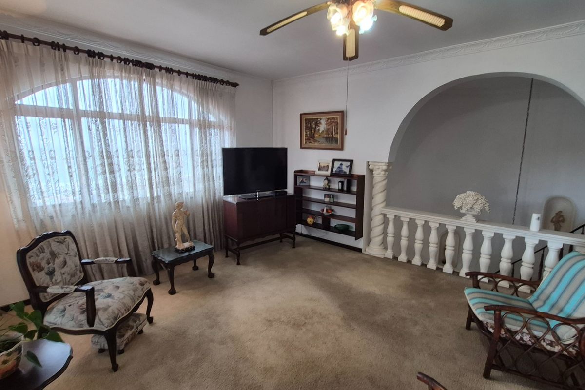 A living room featuring an arched opening with decorative balustrade and columns, crown molding, and a ceiling fan.