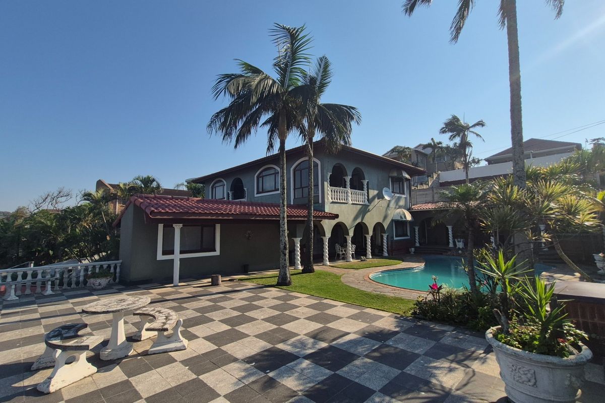 Rear view of the property featuring a swimming pool, expansive tiled patio area, arched architectural details, and a balcony overlooking the garden.