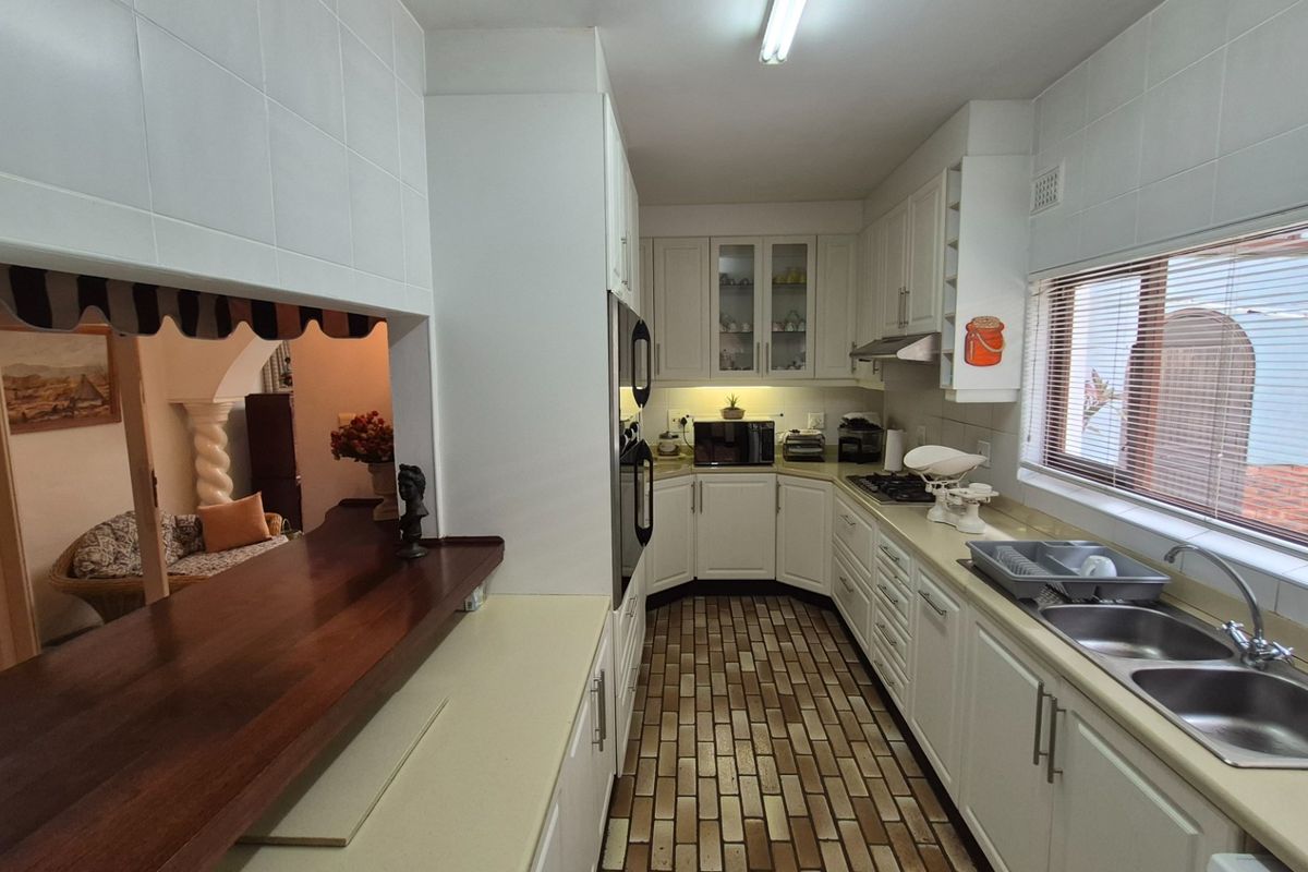 A functional kitchen featuring white cabinetry, a double basin sink, built-in oven, hob, and a breakfast bar overlooking the adjacent living area.