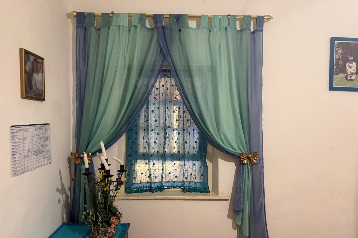 A simple bedroom interior featuring a window with a curtain rod and decorative curtains.