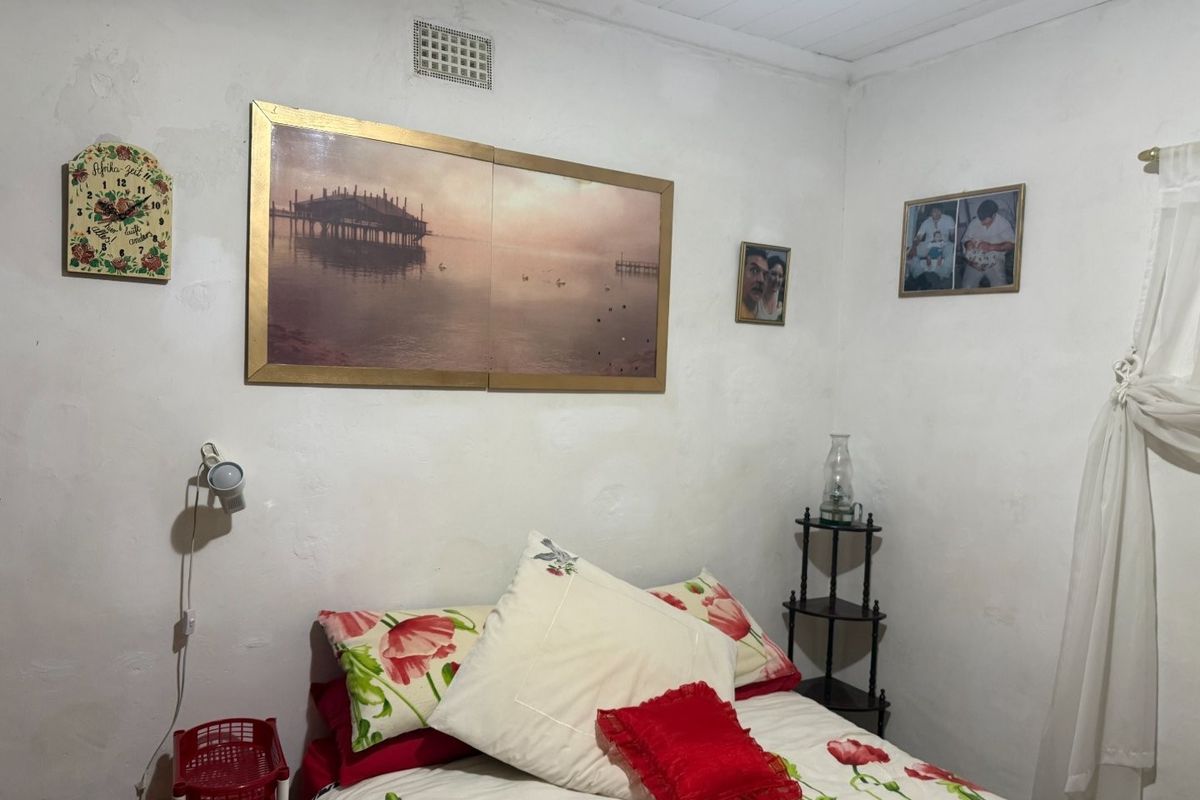 A bedroom featuring white walls with visible texture and a wall-mounted light fixture.
