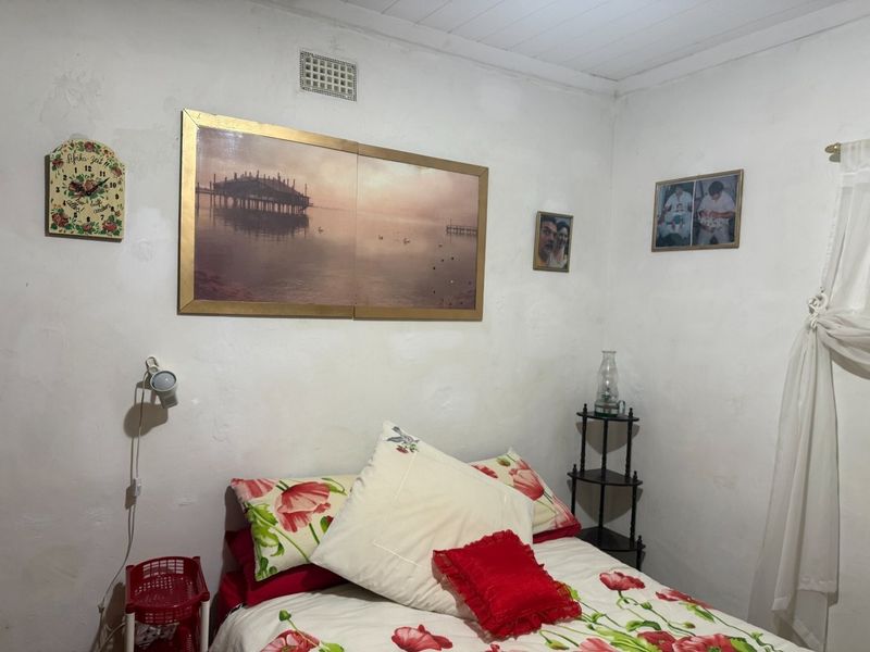 A bedroom featuring white walls with visible texture and a wall-mounted light fixture.