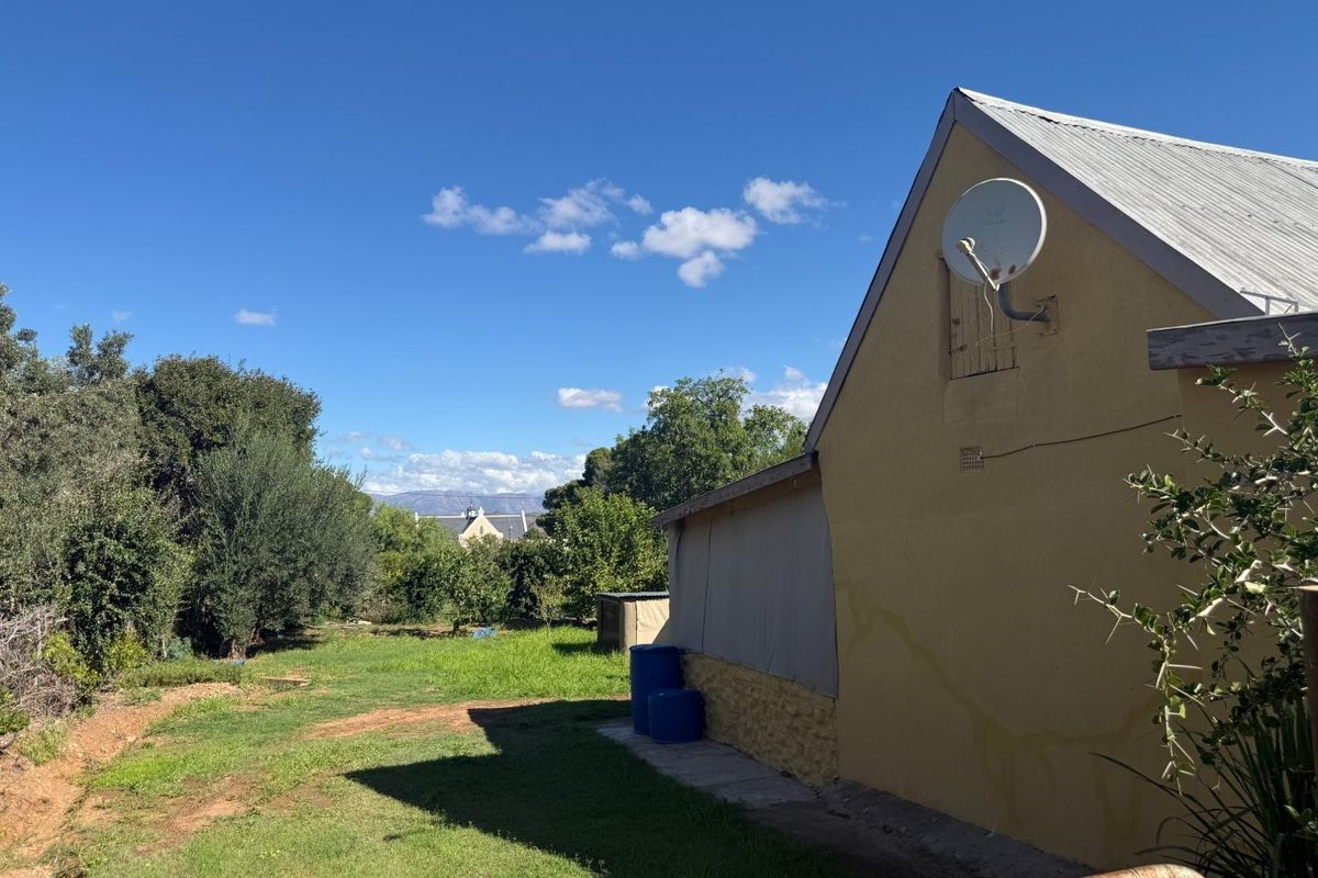 Rear view of the property showing the garden area, corrugated metal roof, and exterior wall with a mounted satellite dish.