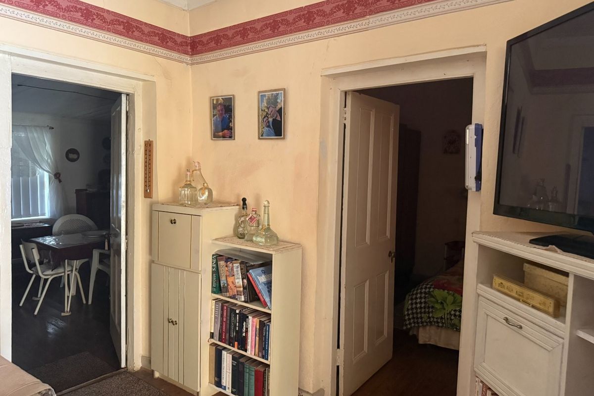 A living area featuring a decorative wallpaper border and timber ceiling, providing access to adjacent rooms through traditional timber doorways.