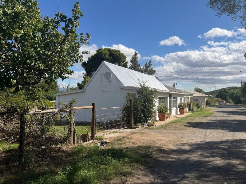 A view of the front exterior of a cottage-style house featuring a metal roof, gravel driveway, and wire fencing.