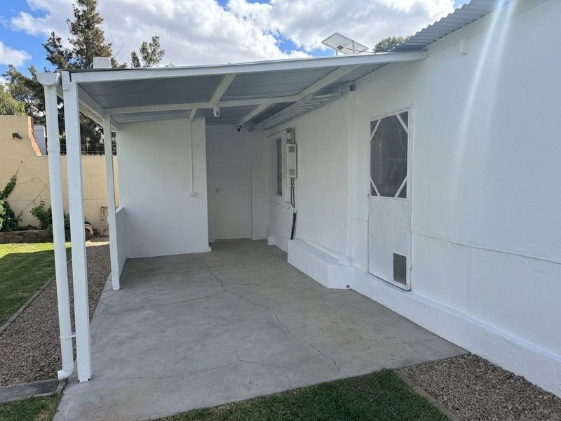 A covered outdoor patio area featuring a concrete slab floor, security screen door, and direct access to the rear garden.