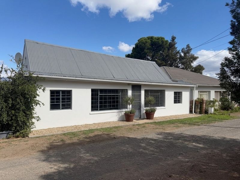 Front exterior view of a single-story house featuring a corrugated metal roof, white rendered walls, and steel-framed windows.