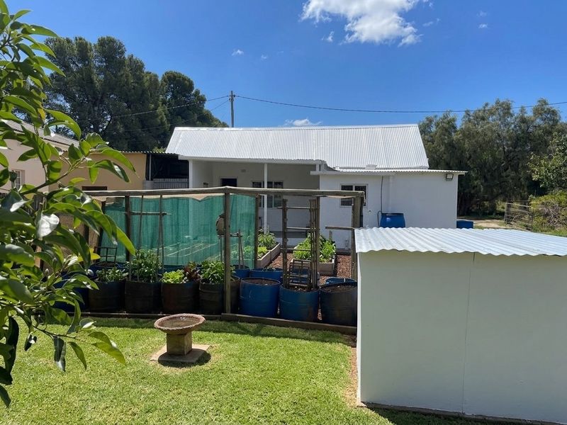 Rear view of the property featuring a white exterior, corrugated metal roofing, a small lawn, and an additional outbuilding structure.