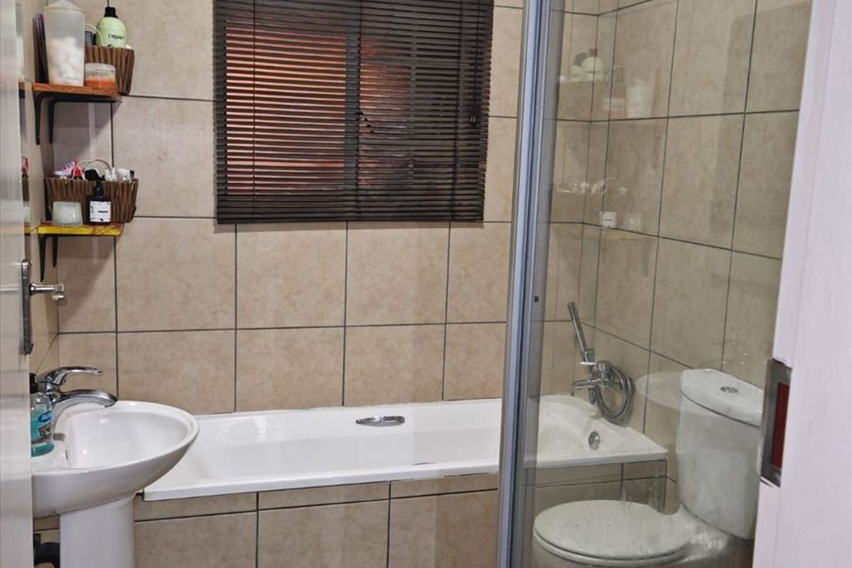 A functional bathroom featuring a pedestal basin, built-in bathtub, separate shower enclosure, and toilet with neutral wall and floor tiling.