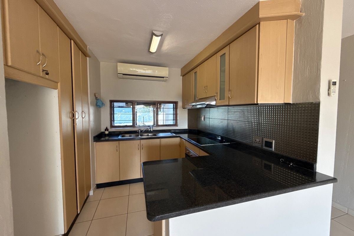 A functional kitchen featuring light wood cabinetry, dark granite countertops, a tiled backsplash, and an integrated electric hob with an extractor fan.