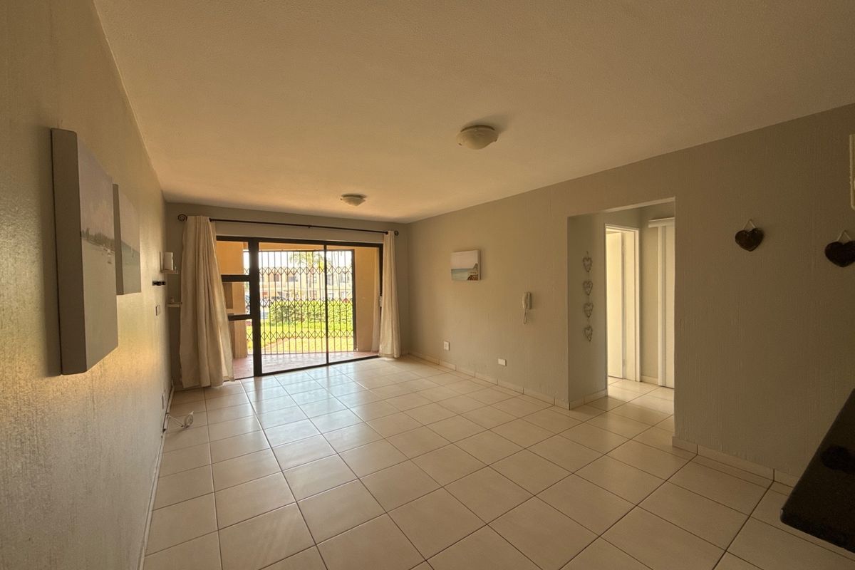 An open-plan living area featuring neutral tiled flooring, a sliding glass door with security gate, and direct access to an outdoor patio space.