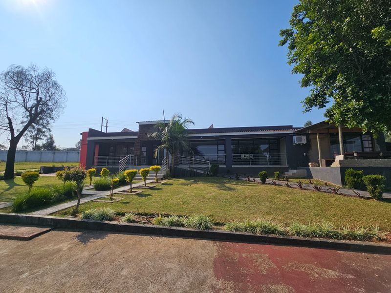 Front view of a modern single-story house featuring a landscaped lawn, paved driveway, and a raised patio area with metal railings.