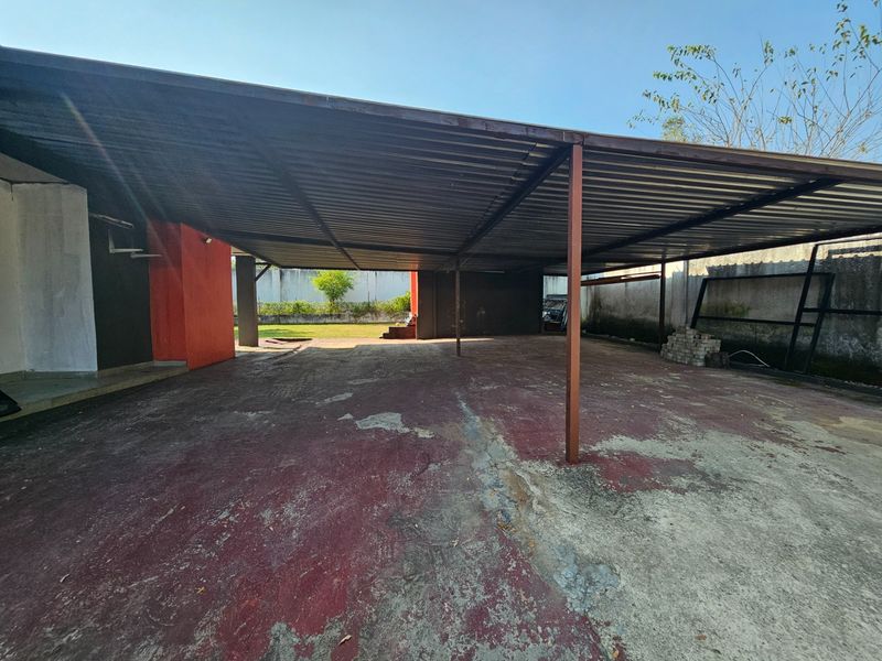 A spacious, covered outdoor parking area or garage featuring a metal roof structure and concrete flooring, requiring maintenance and surface restoration.