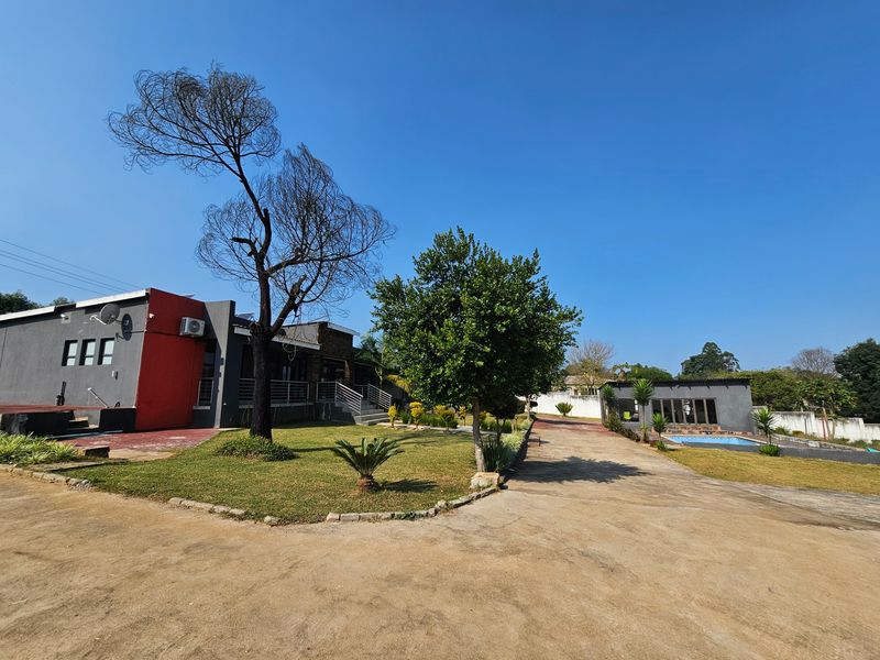 Spacious rear exterior view featuring a large paved driveway, landscaped garden, swimming pool, and multi-level building structure with modern facade accents.