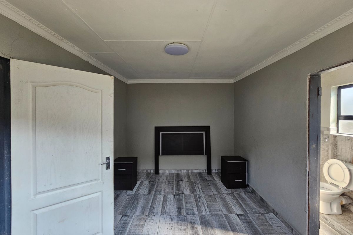 A bedroom featuring wood-look tiled flooring and ceiling cornicing, with an adjacent bathroom visible through the doorway.