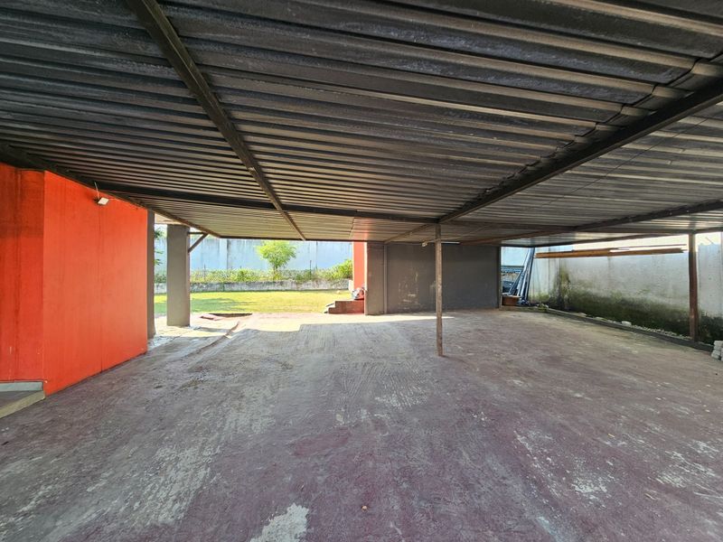 A spacious, covered outdoor garage or utility area featuring a corrugated metal roof, concrete flooring, and direct access to the rear garden.