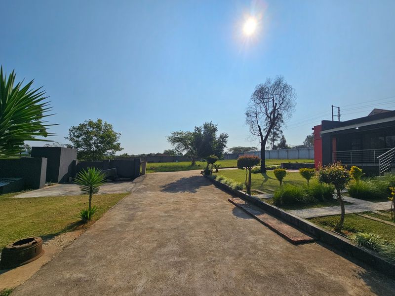 A wide view of the property entrance featuring a concrete driveway, landscaped garden areas, and a boundary wall under a clear sky.