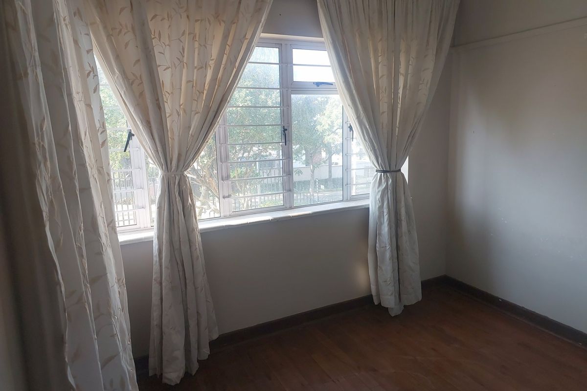 An empty bedroom featuring timber flooring, large windows with security bars, and neutral wall finishes, offering a blank canvas for potential interior design updates.