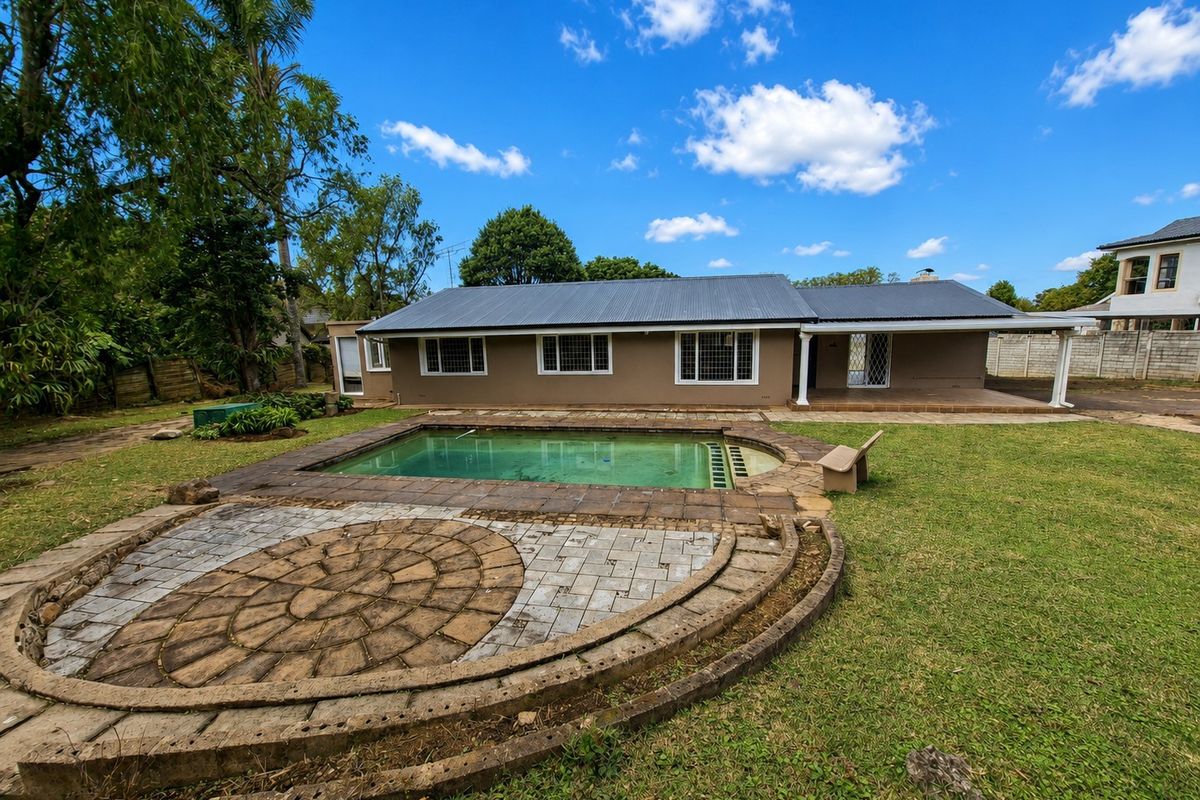 Rear view of the property featuring a swimming pool, circular paved patio area, covered veranda, and a spacious garden with a metal roof structure.