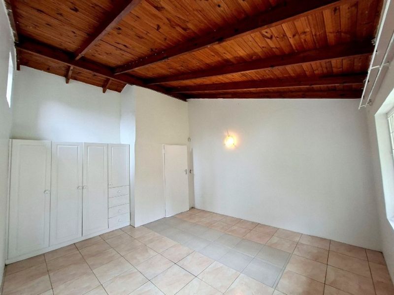 A spacious bedroom featuring exposed timber beam ceilings, tiled flooring, and built-in storage cupboards, offering a neutral canvas for interior design.