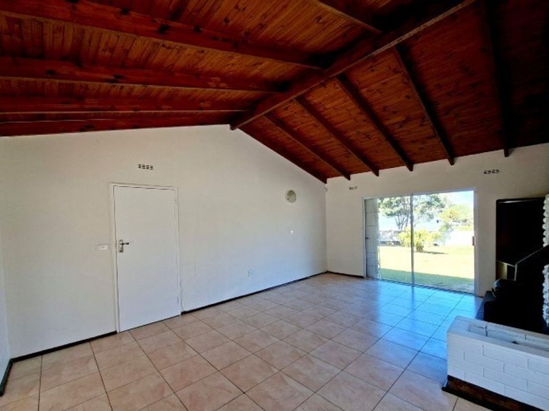 Spacious living area featuring exposed timber rafter ceilings, tiled flooring, a brick fireplace, and sliding glass doors leading to the garden.