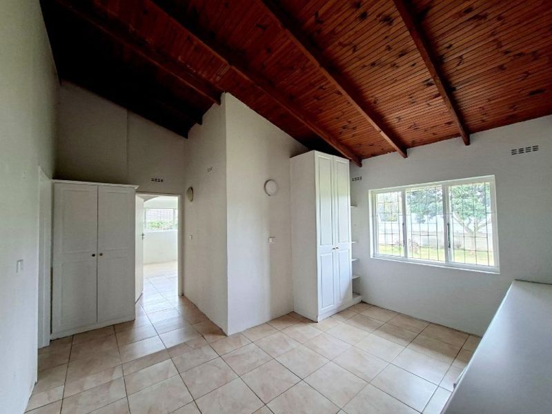 A spacious bedroom featuring exposed timber rafter ceilings, tiled flooring, and built-in storage cupboards with security bars on the windows.