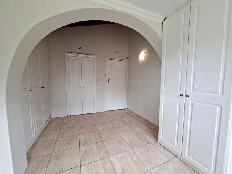 A spacious hallway featuring neutral tiled flooring, an architectural archway, and extensive built-in cupboard storage.