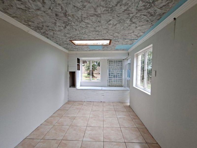 An empty living room featuring tiled floors, a built-in window seat, and a skylight. The ceiling requires repair and cosmetic updates.