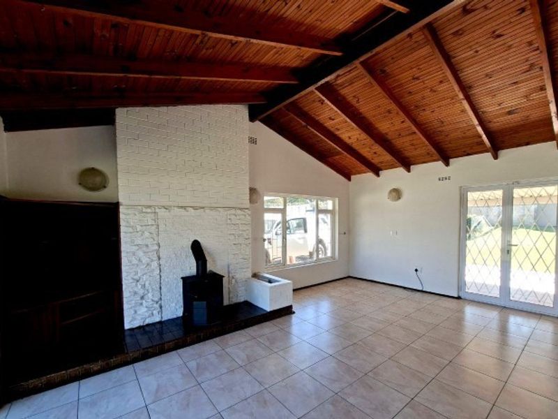 Spacious living room featuring a vaulted timber ceiling, a white brick fireplace with a wood-burning stove, tiled floors, and access to the garden.
