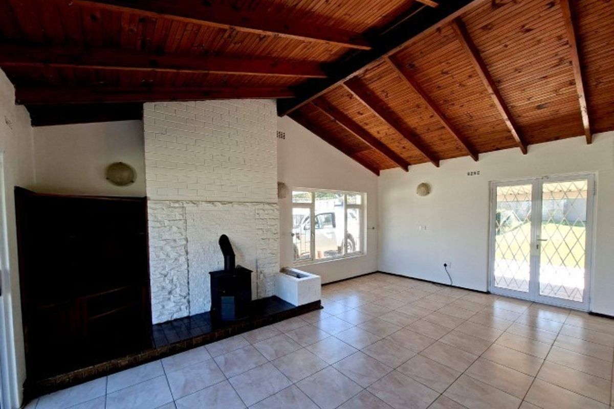 Spacious living room featuring a vaulted timber ceiling, a white brick fireplace with a wood-burning stove, tiled floors, and access to the garden.