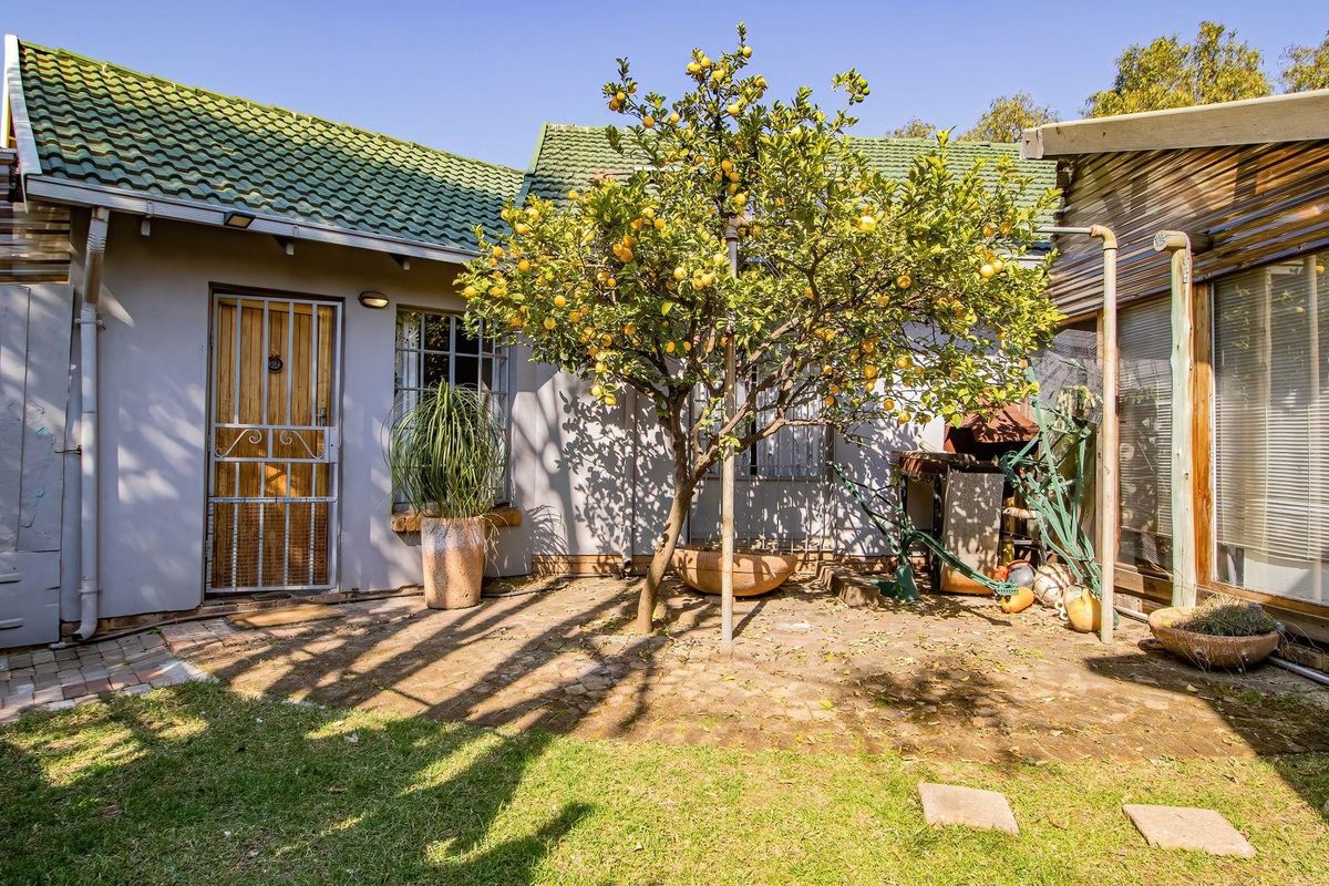 A rear courtyard area featuring a paved patio, established fruit tree, and direct access to the home via a security gate.