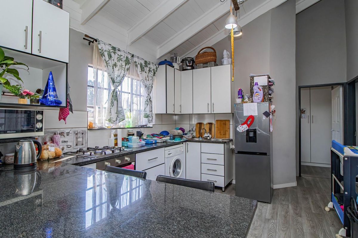 Functional kitchen featuring granite countertops, white cabinetry, gas hob, and an integrated washing machine under a high exposed beam ceiling.