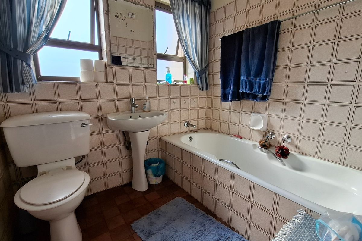 A dated bathroom featuring a pedestal basin, bathtub, and toilet with original tiled finishes, offering potential for a modern renovation.