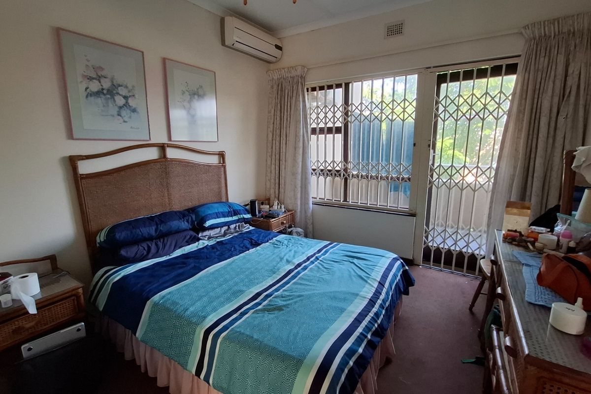 A bedroom featuring carpet flooring, a split-system air conditioner, and a sliding glass door with a security gate leading to an outdoor area.